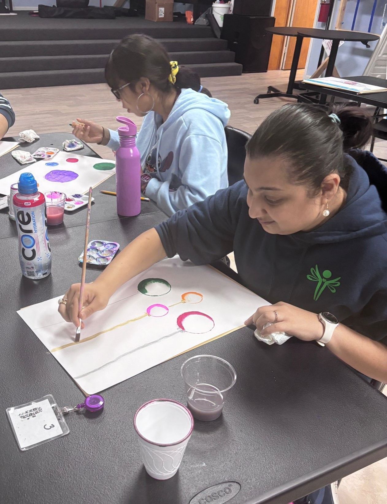 A woman is sitting at a table painting with a brush.
