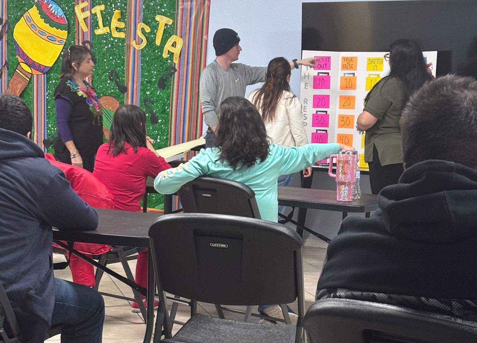 A group of people are sitting at tables in front of a sign that says fiesta