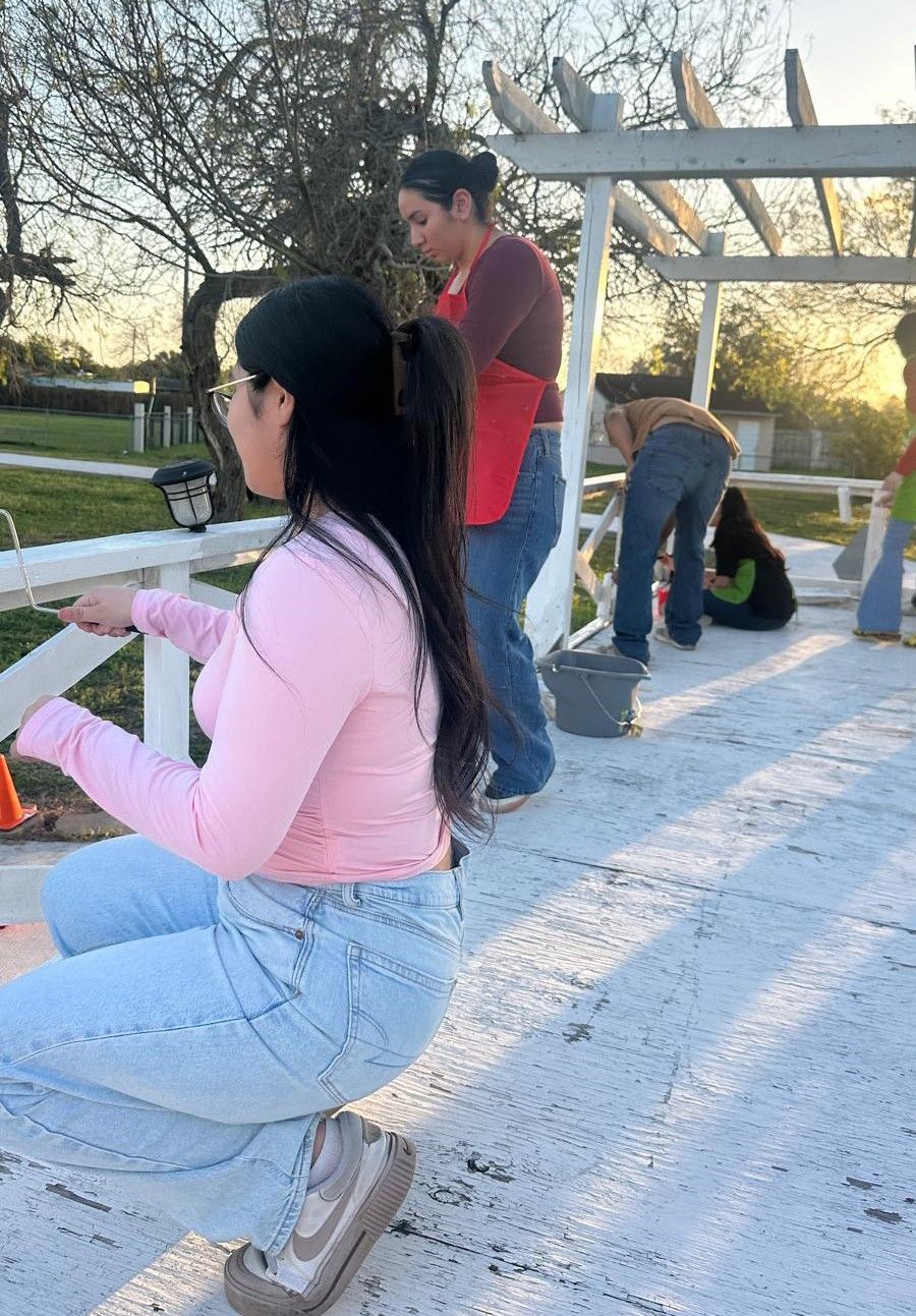 Woman in pink top and jeans squats, working outdoors with others.