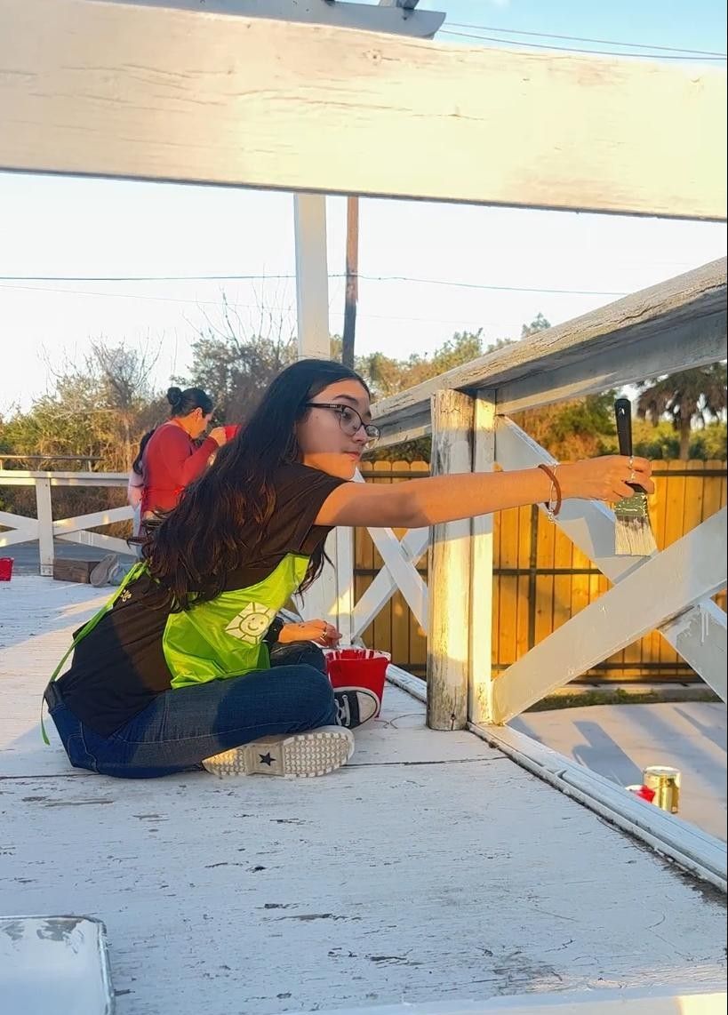 Woman painting white fence outdoors.