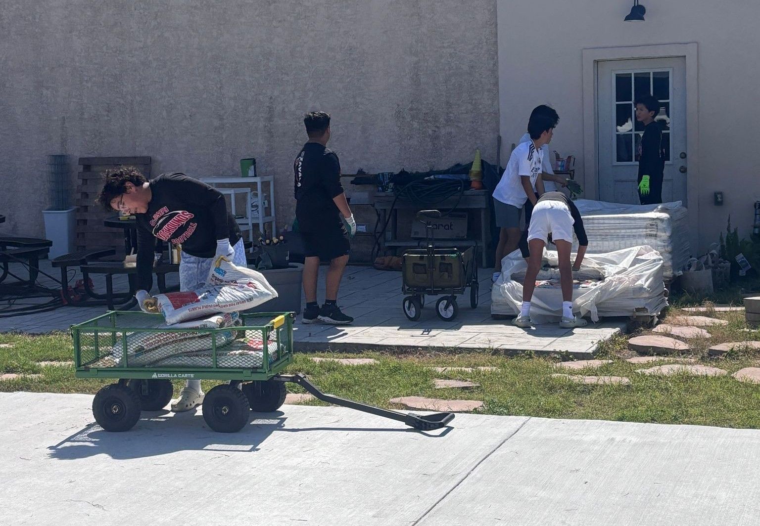 Group of teens unloading supplies from a green wagon in front of a building.