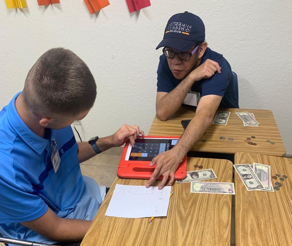 Two men are sitting at a table with money and a tablet
