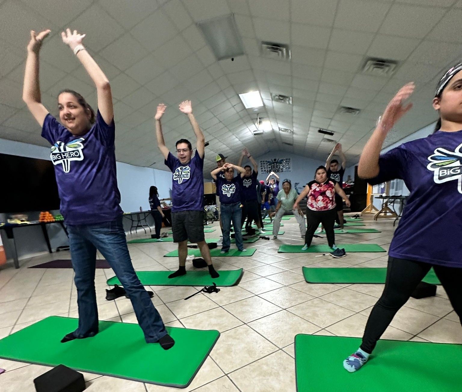 A group of people in purple shirts are doing yoga on green mats