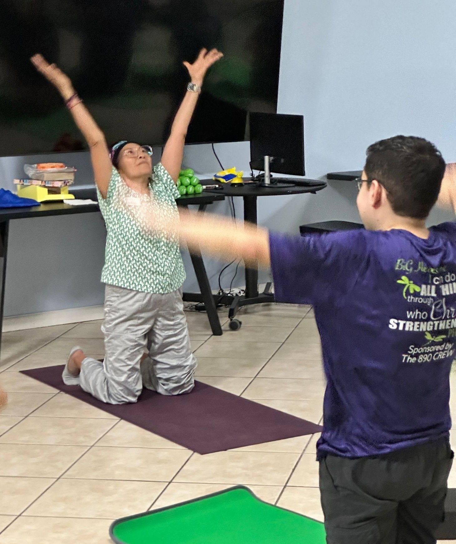 A man in a purple shirt stands next to a woman on a yoga mat