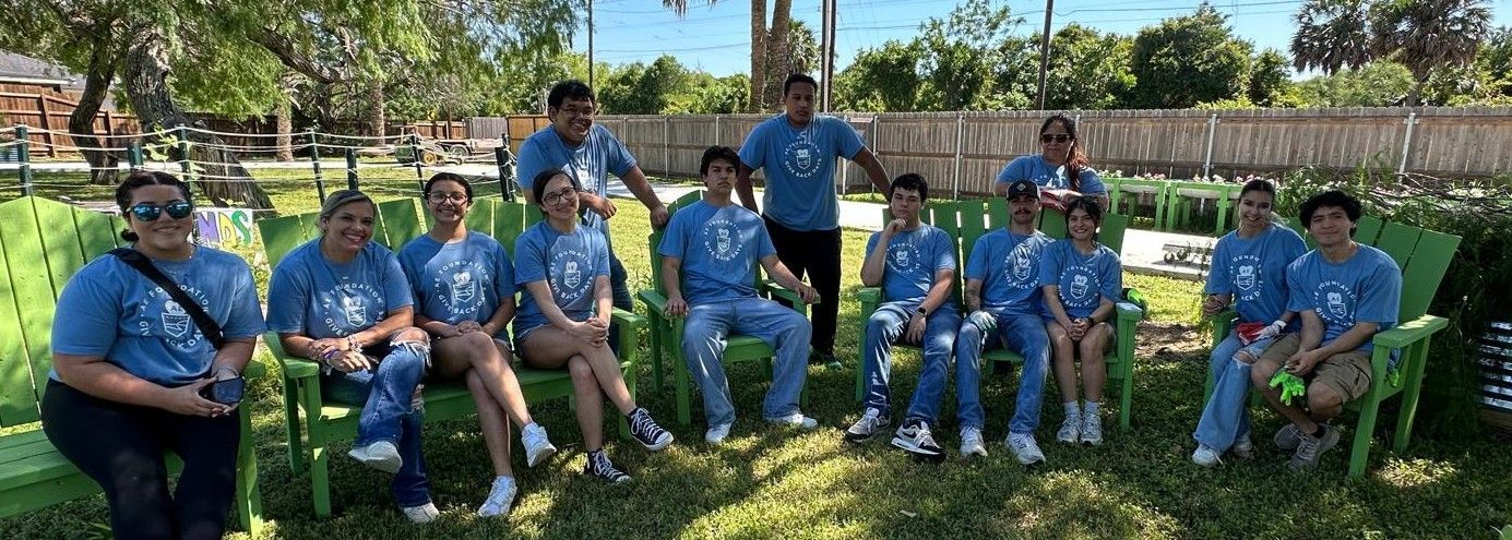 Group of people in blue t-shirts sitting and standing outside on green chairs.