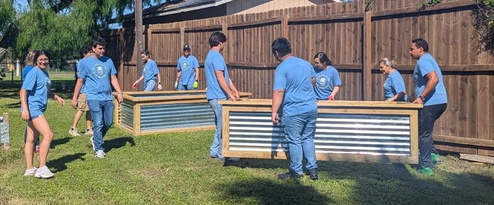 Group of people in blue shirts assembling garden beds on grass.