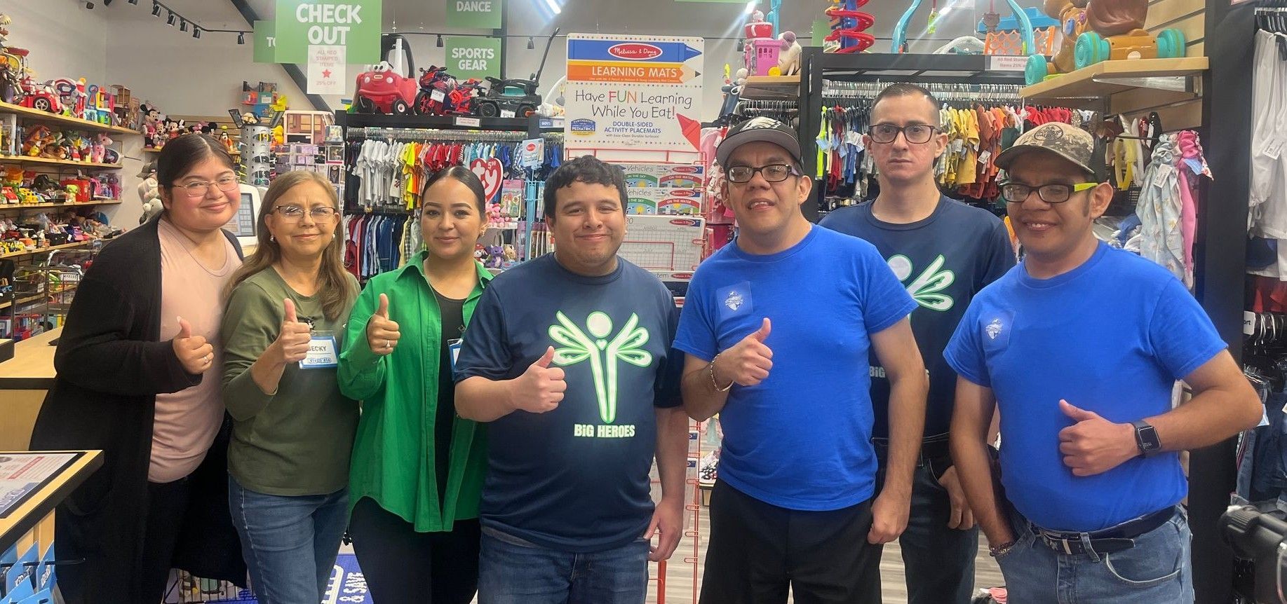 Group of people giving thumbs up in a store. Some are wearing blue shirts.