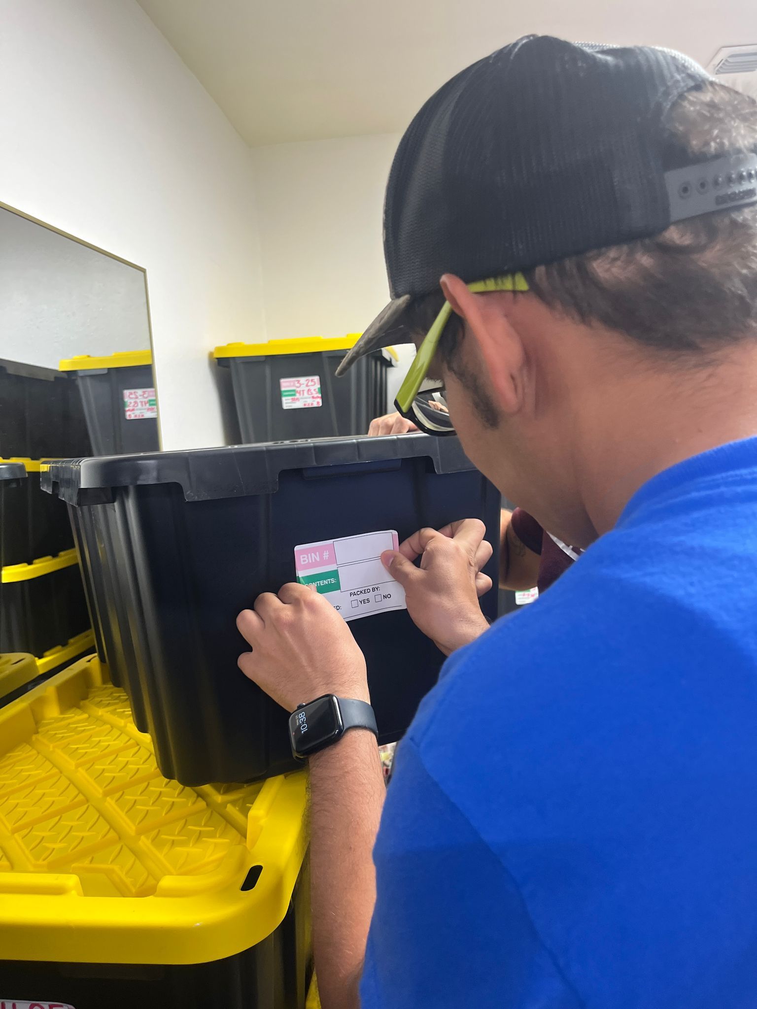 Person in blue shirt applying a label to a black storage bin on a yellow bin.