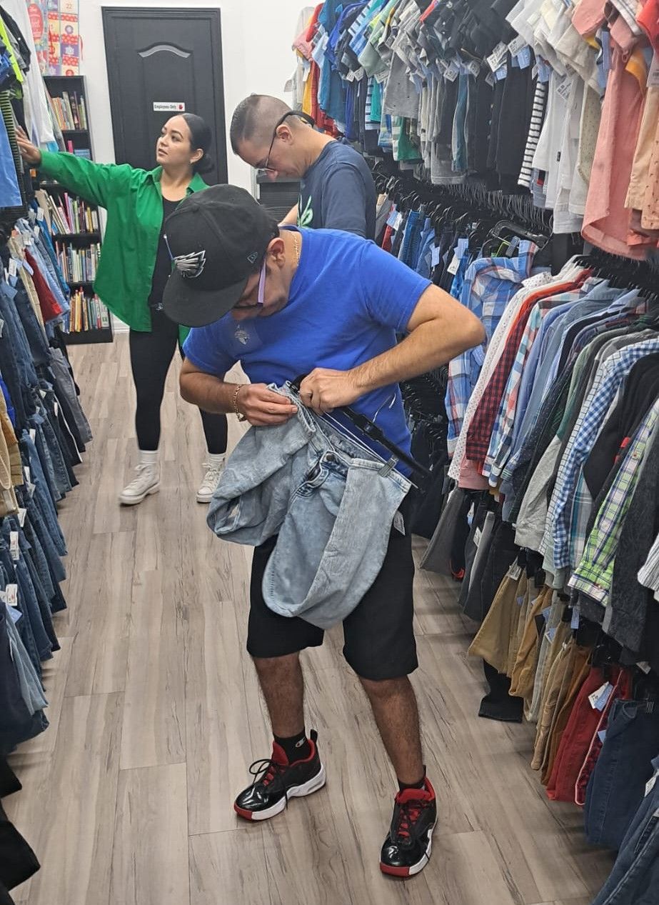 People browsing clothes in a store. A man inspects jeans; another looks at a rack; a woman points.