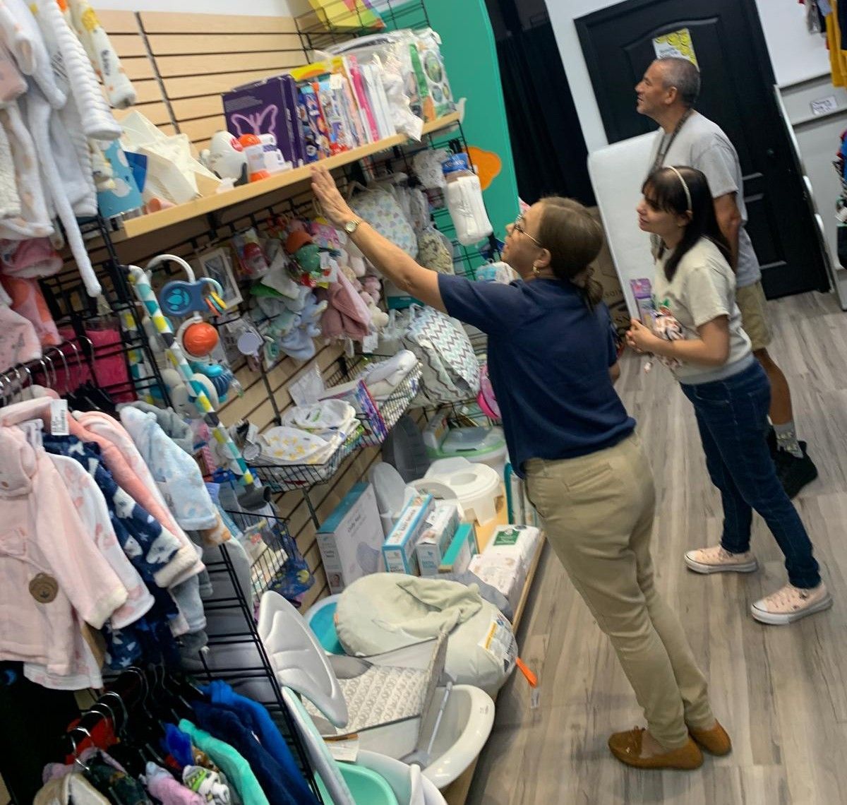 Woman reaching for item on shelf in store. A man and girl look on.