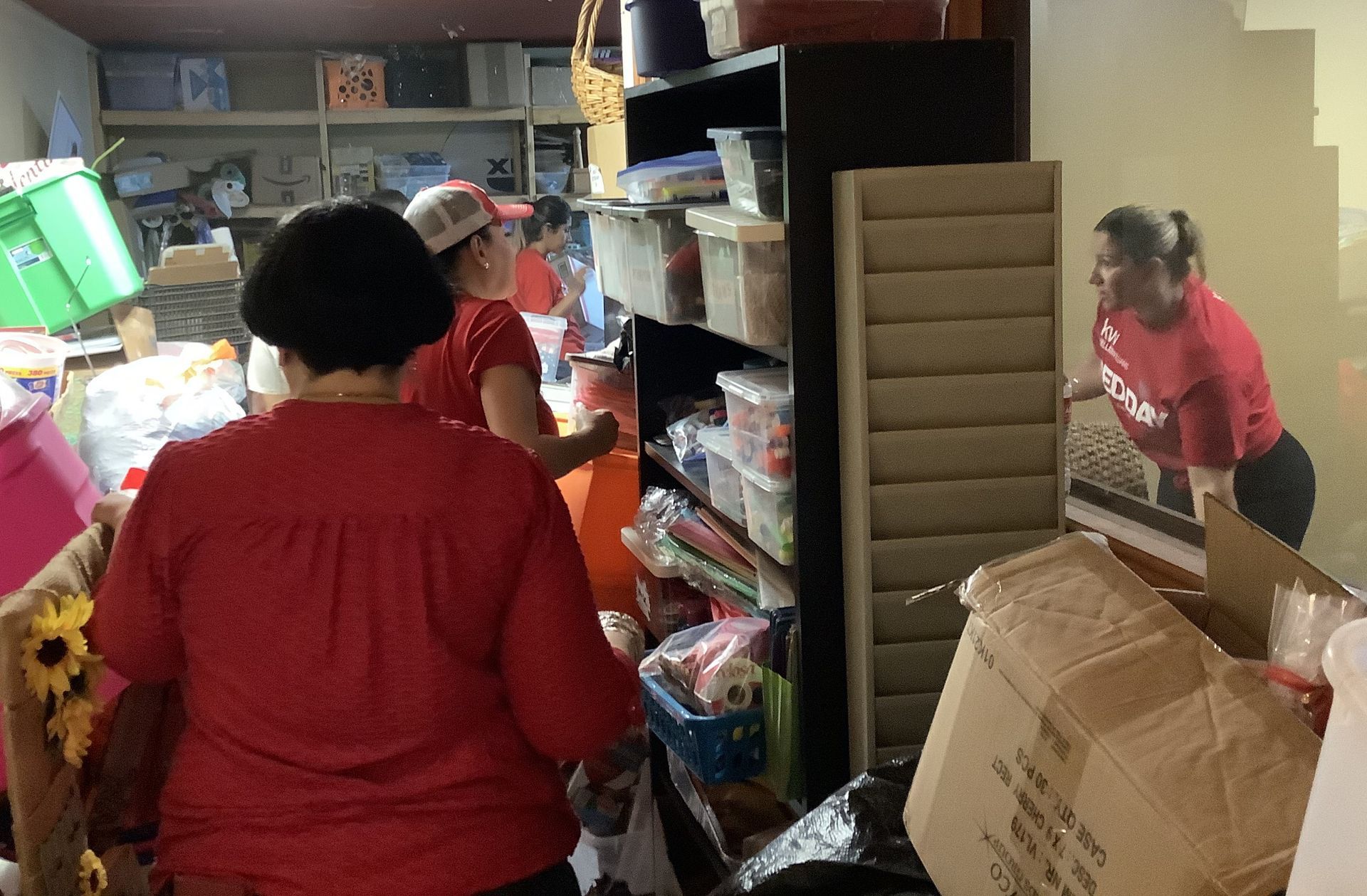 A woman in a red shirt is standing in a room filled with boxes.