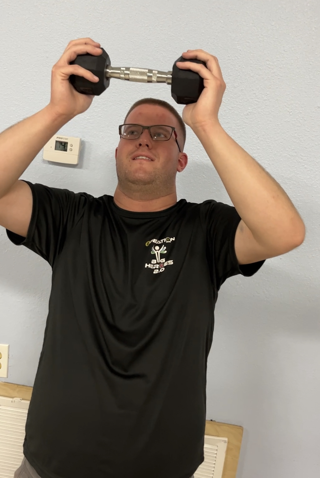 A man wearing glasses holds a dumbbell over his head