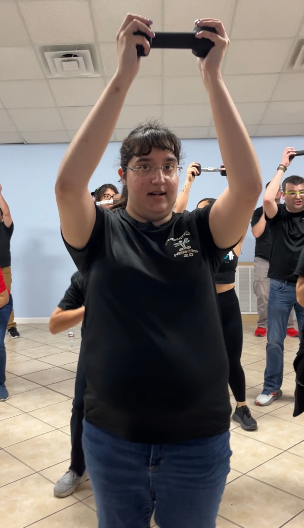A group of people are standing in a room holding dumbbells over their heads.