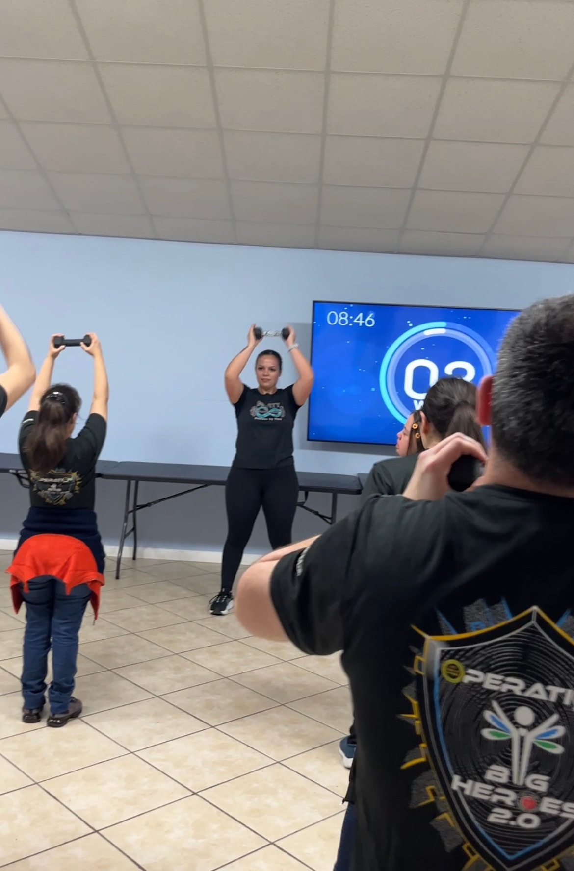 A group of people are doing exercises with dumbbells in a room.