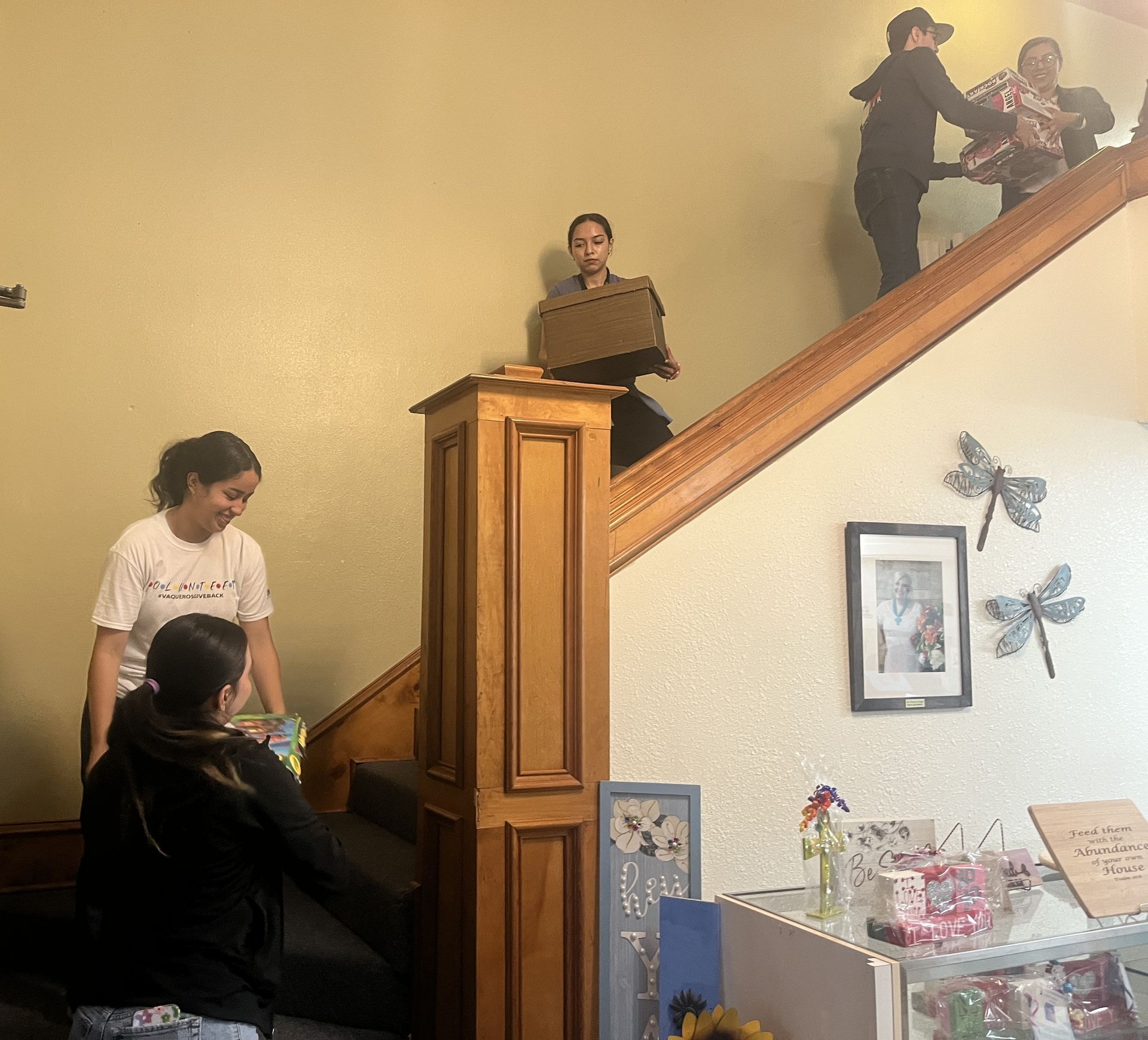 People carrying boxes up and down a wooden staircase. Retail shop setting.