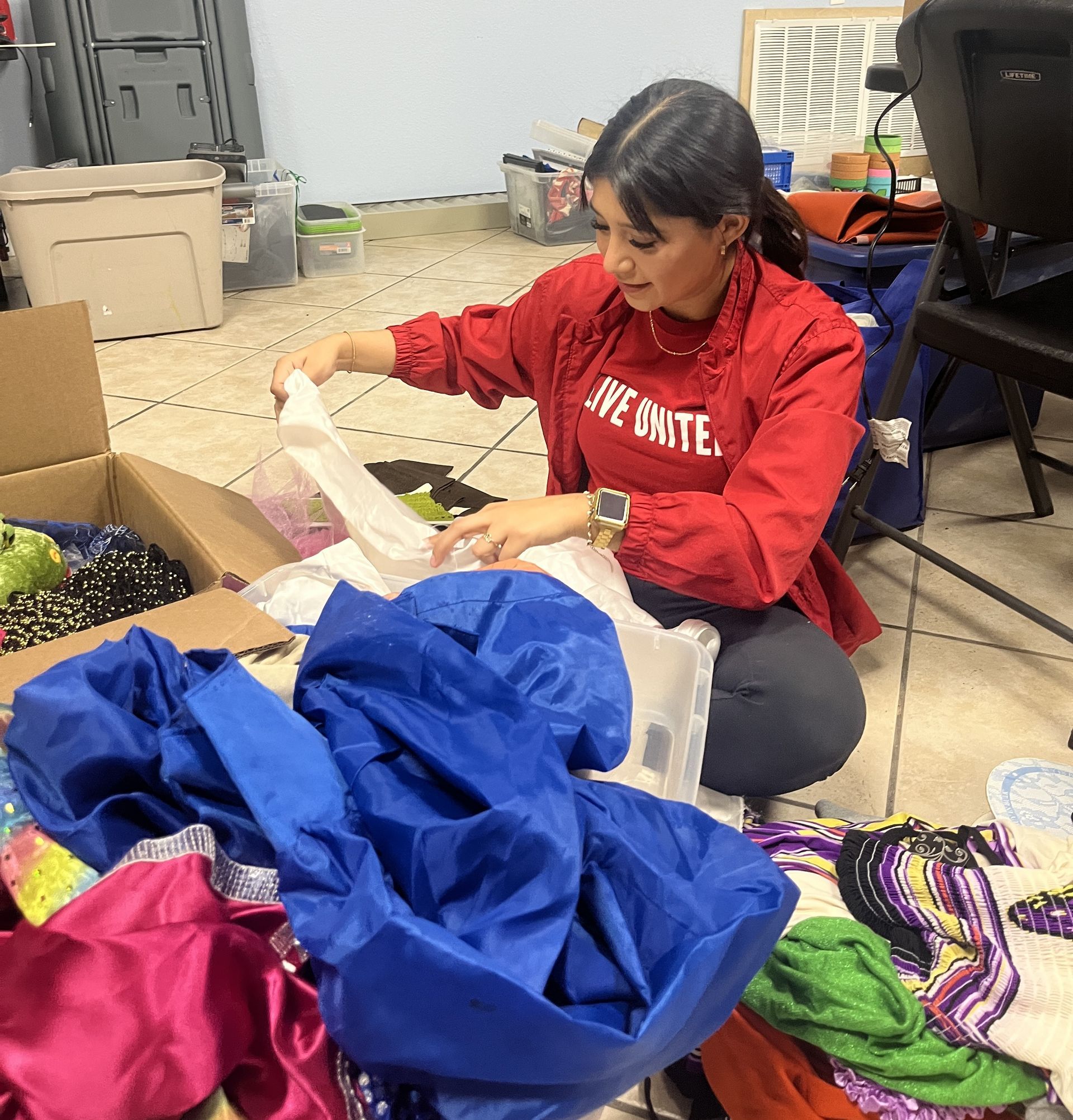 Woman in red sorting through donations on the floor, surrounded by colorful clothing.