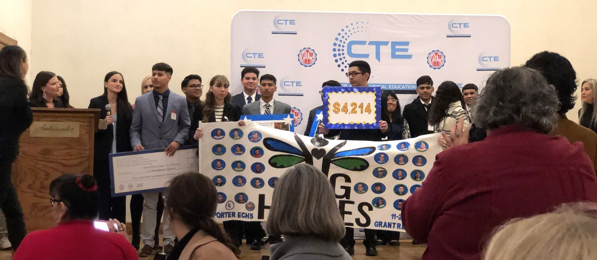 A group of students at an event hold a banner and a check that says $4,214, CTE backdrop.