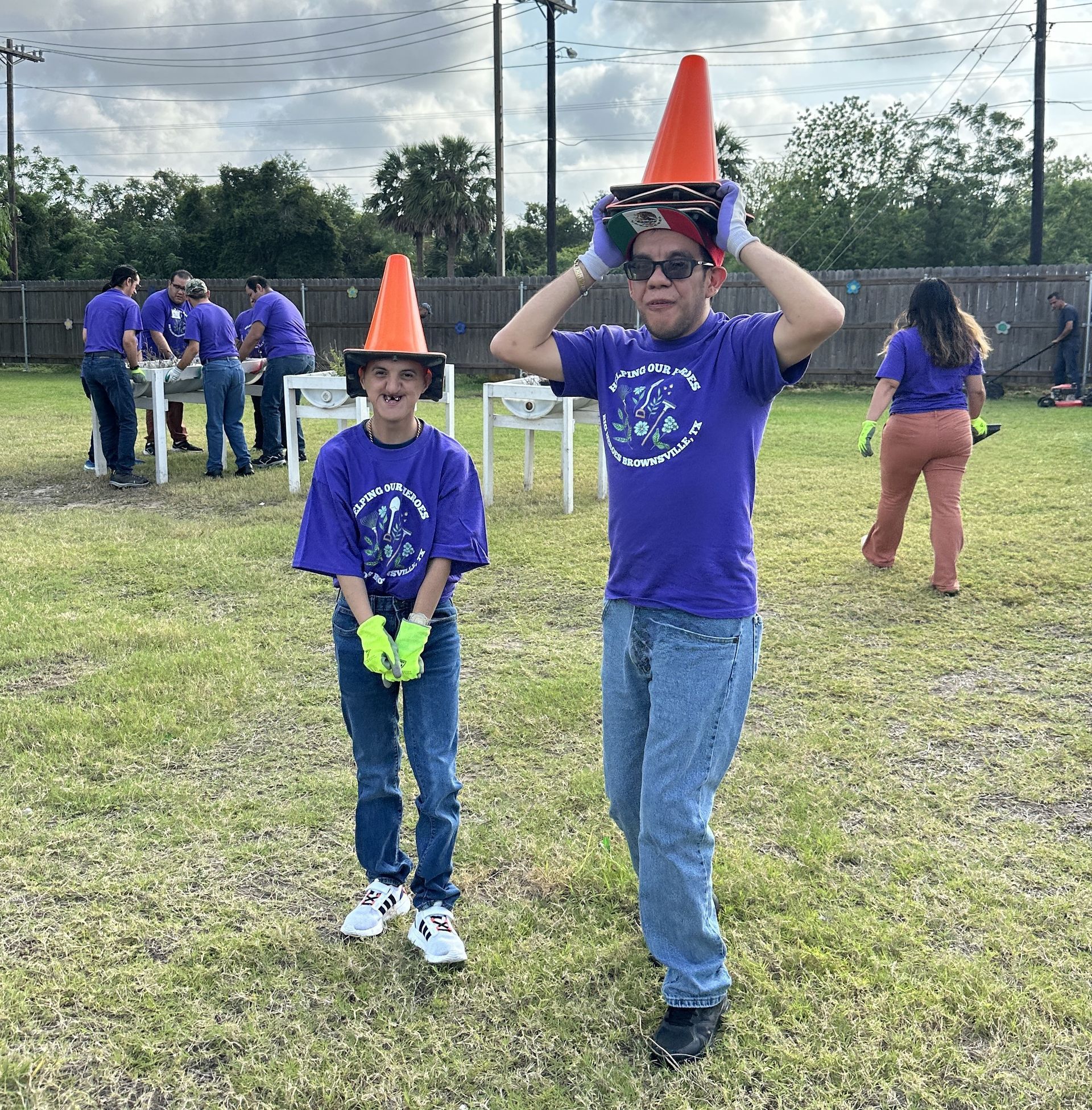 Two children wearing purple shirts and orange cones are standing in a field.