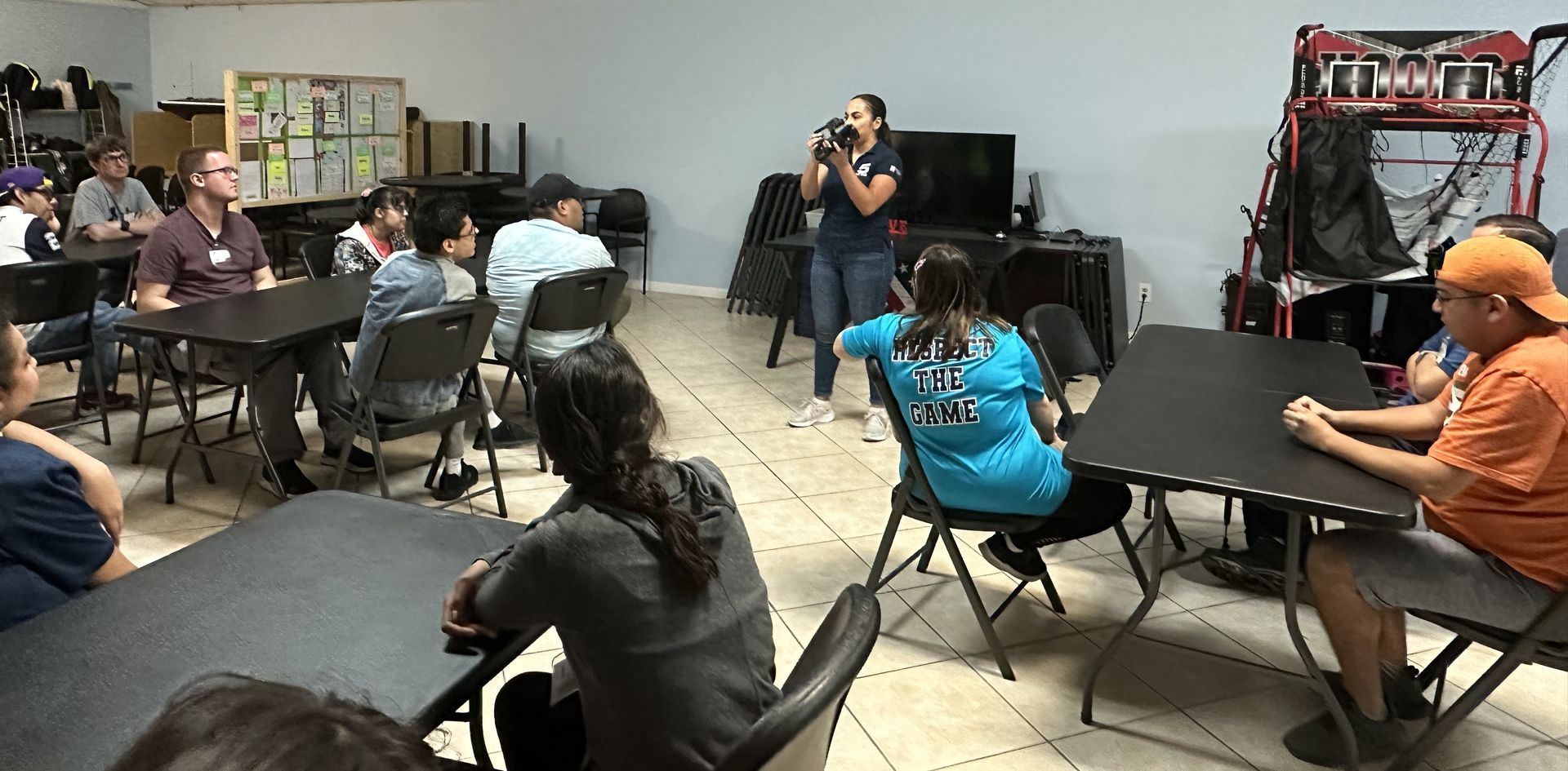 A man is standing in front of a group of people sitting at tables.
