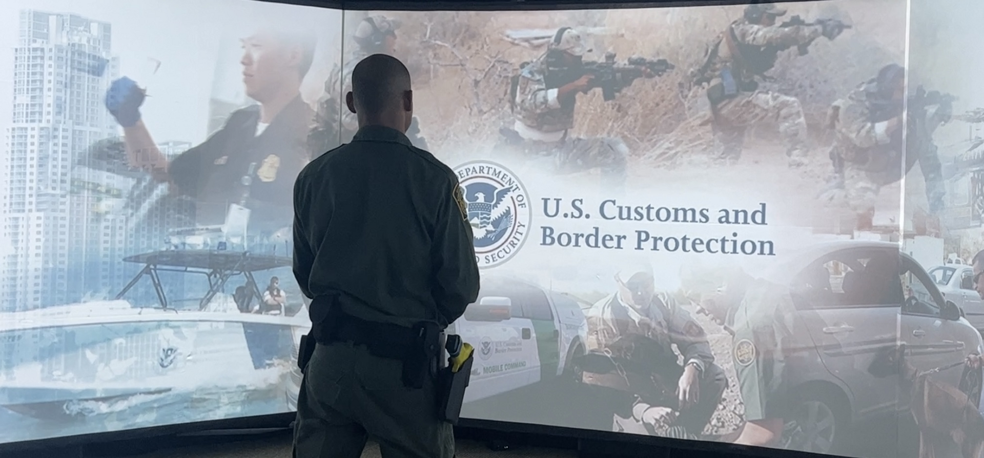 A man is standing in front of a screen that says u.s. customs and border protection.