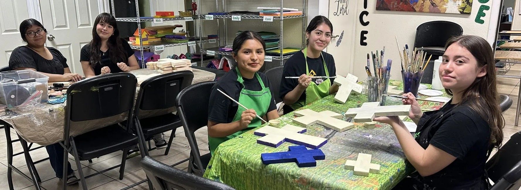 People painting wooden crosses at a table covered in a green tablecloth.