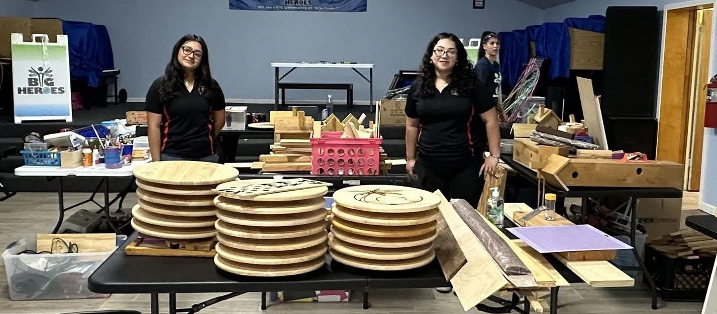 Two women standing behind a table with stacks of wooden discs. Indoors.