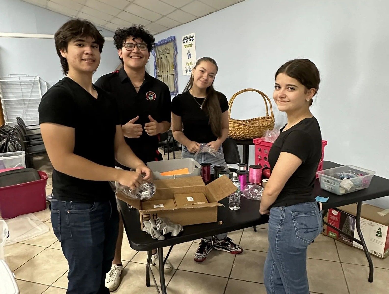 Four young people sort items at a table. Inside, two boys and two girls.