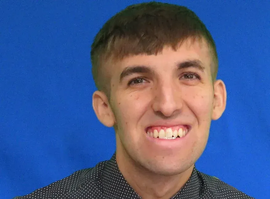 A young man is smiling for the camera in front of a blue background.