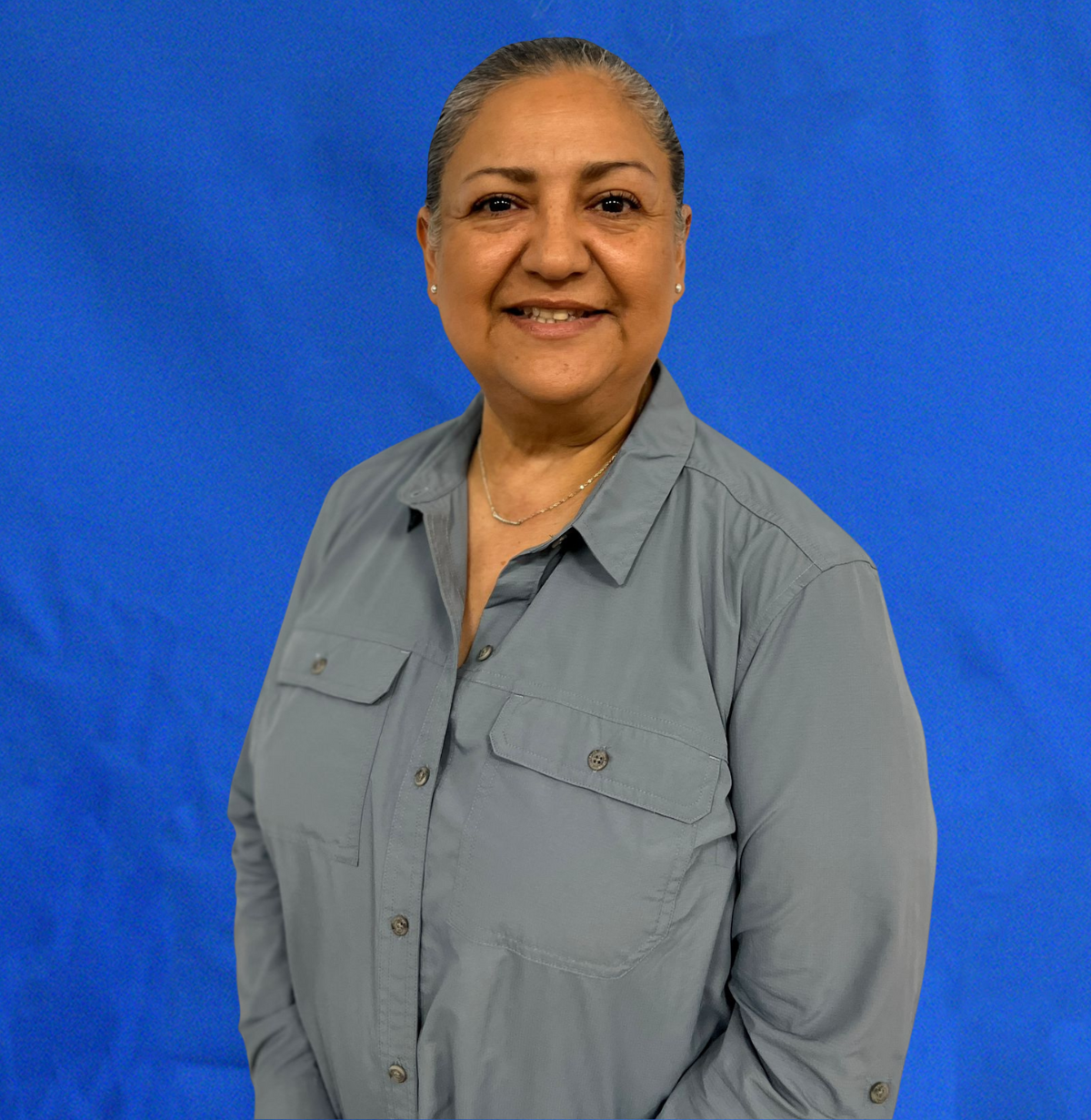 Woman with gray shirt smiling against a blue backdrop.