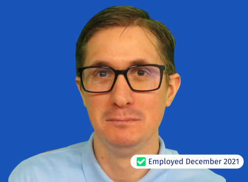 A man wearing glasses is standing in front of a blue background.