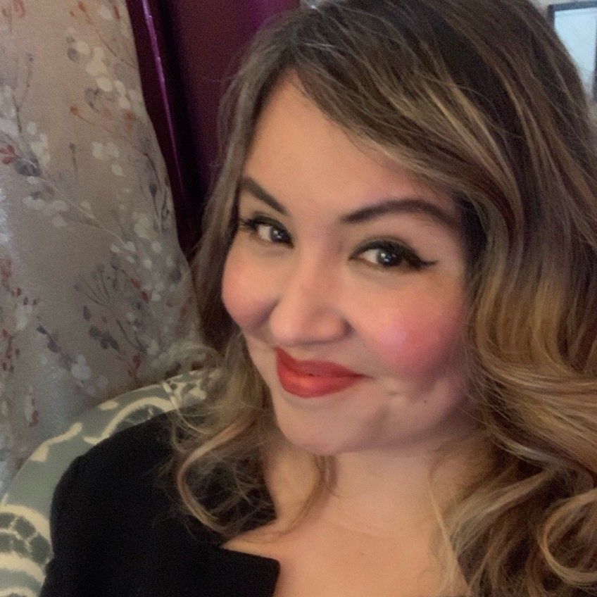 A woman wearing a black shirt and red lipstick is smiling for the camera.