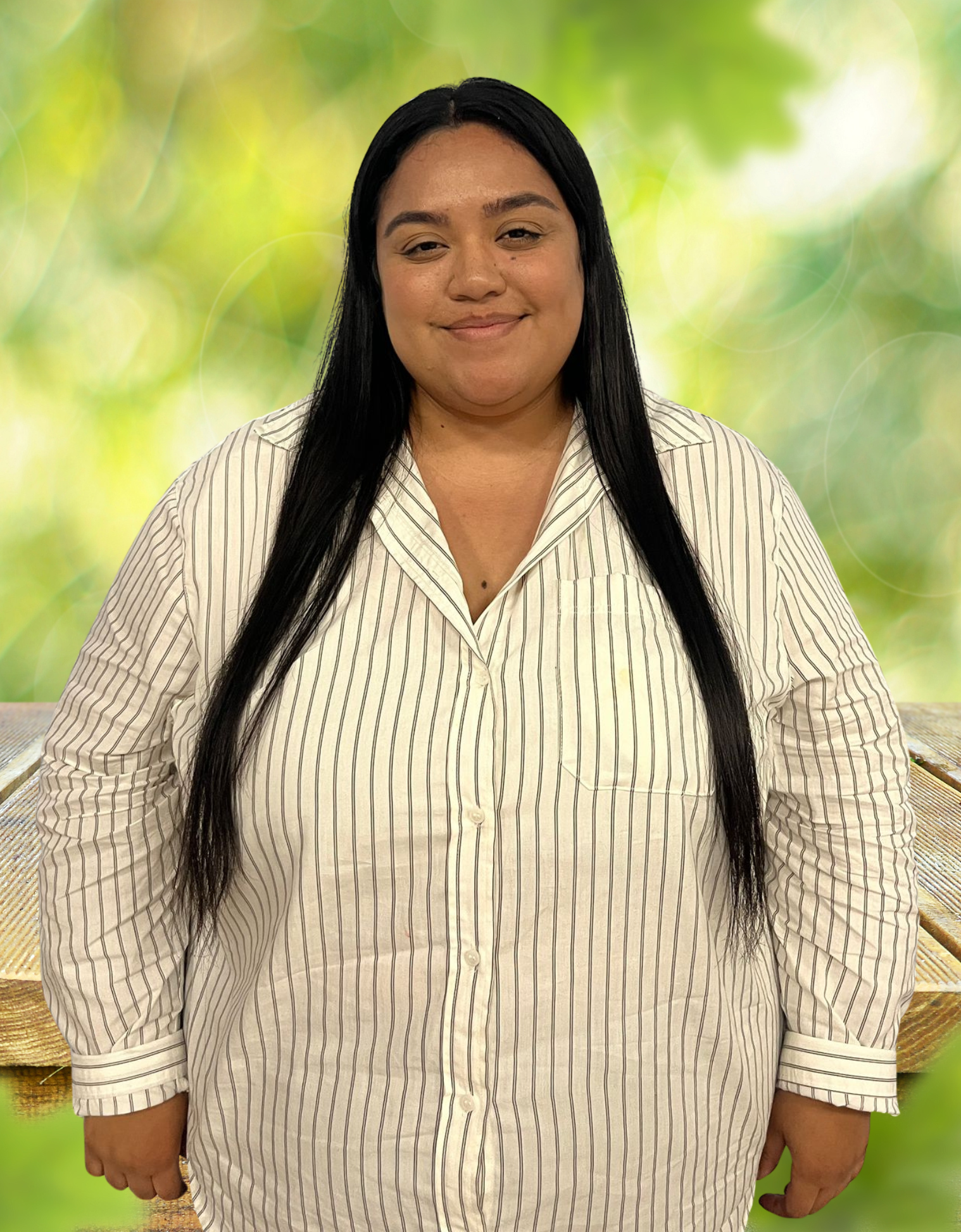 Woman with long black hair, wearing a striped button-up shirt, smiles, outdoors.
