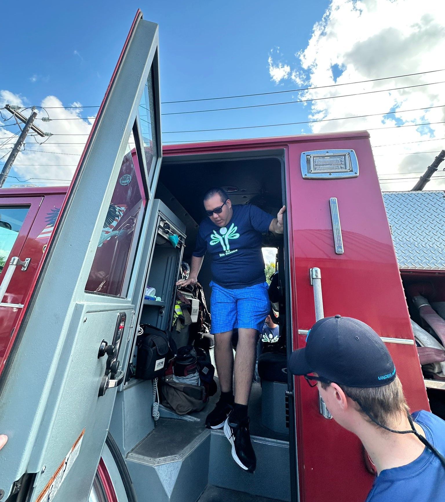 A man in a blue shirt is getting out of a red fire truck.