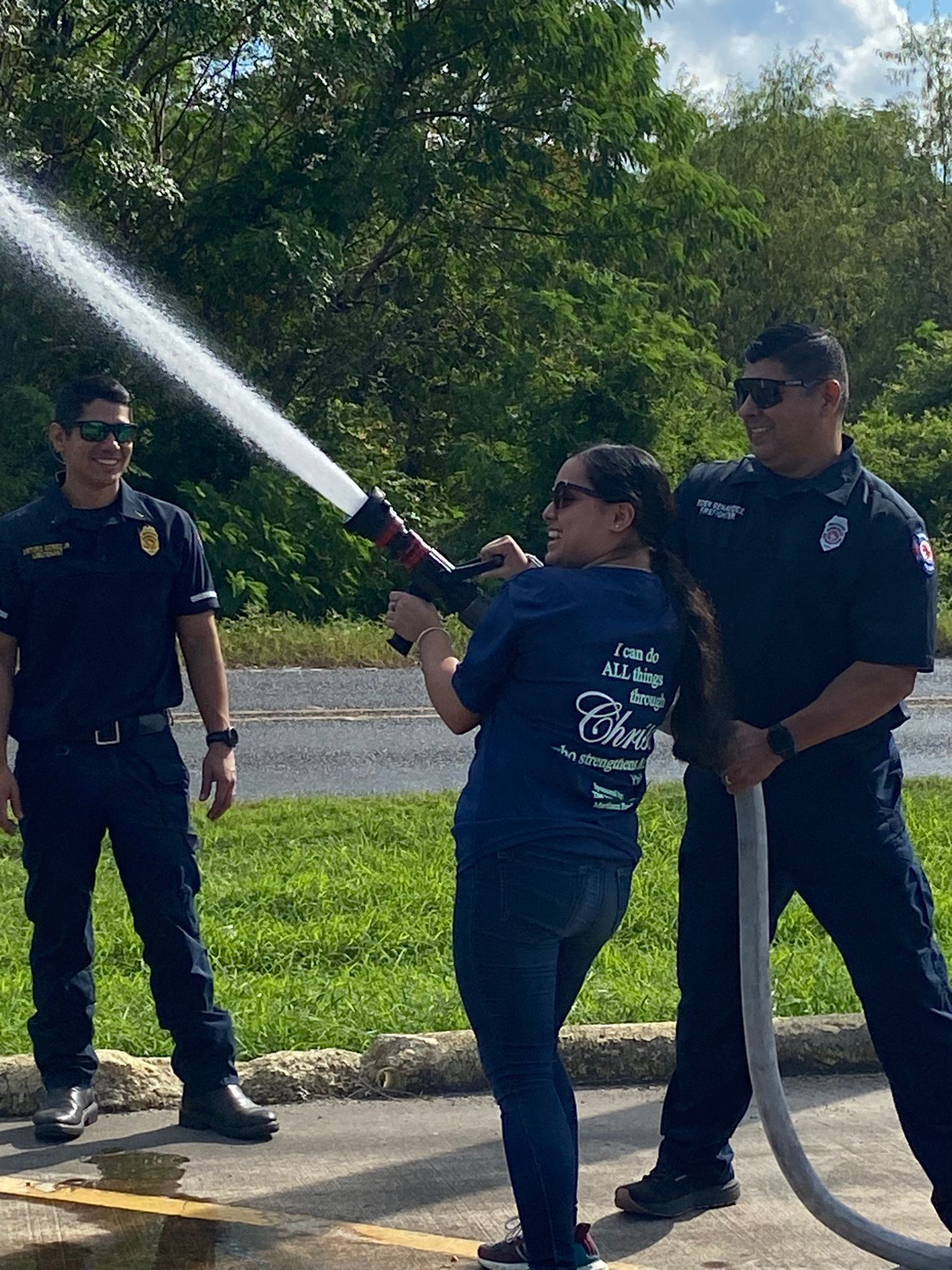A woman is spraying water from a fire hose while two men stand behind her.