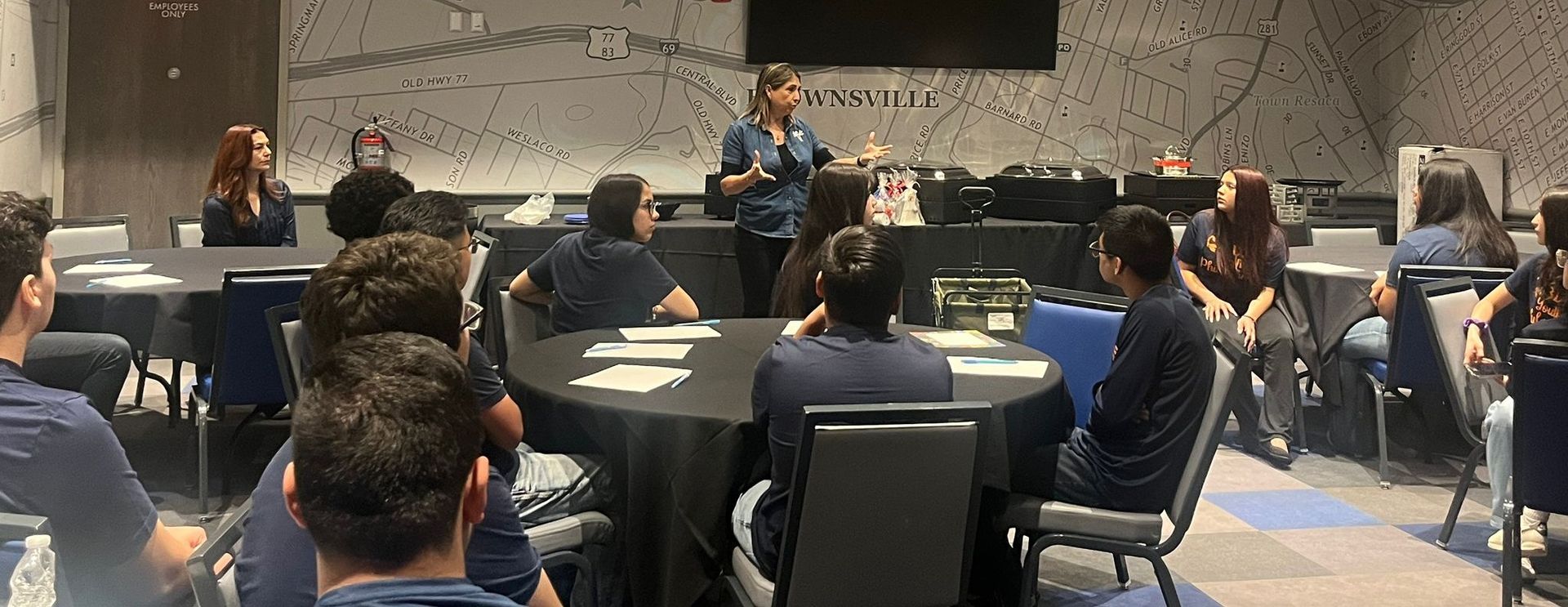 A woman giving a presentation to a group of people seated at tables in a conference room.