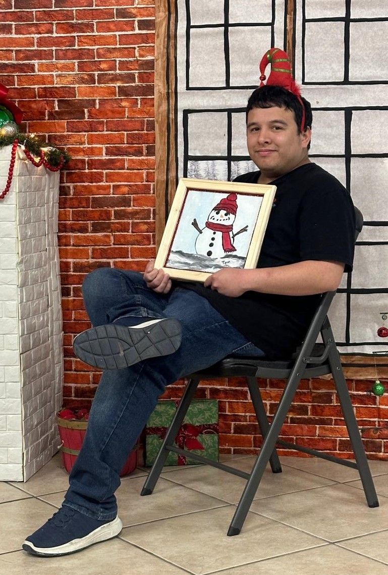 A man is sitting in a chair holding a picture of an elf on the shelf.