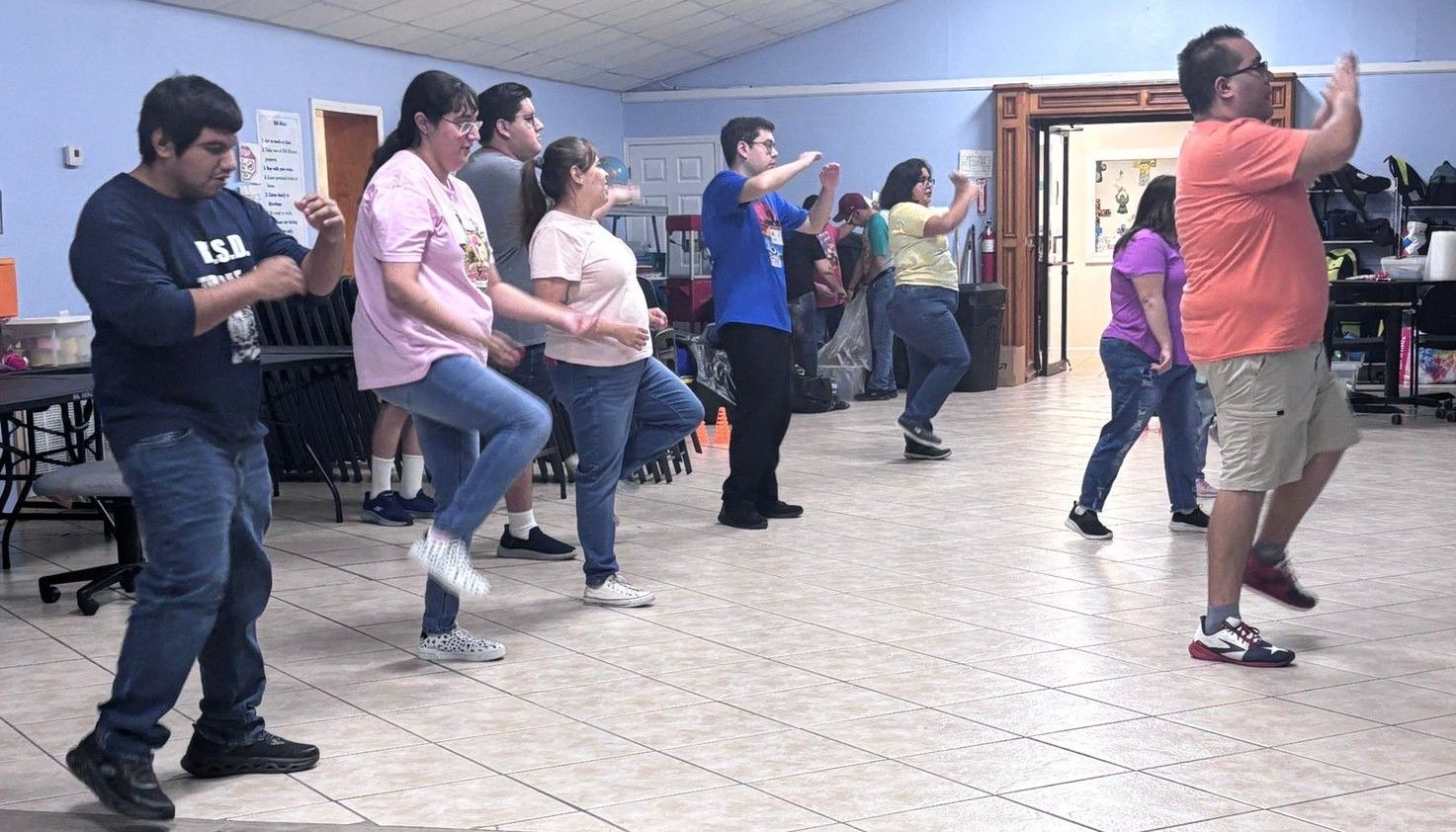 People of various ages in casual clothes doing an exercise routine in a room.