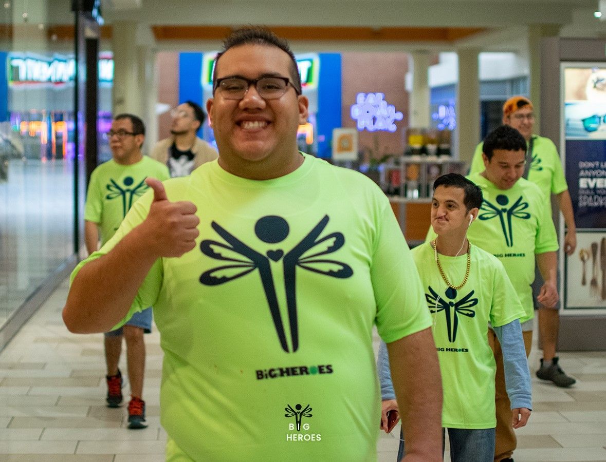 A man wearing a green shirt with a dragonfly on it is giving a thumbs up.
