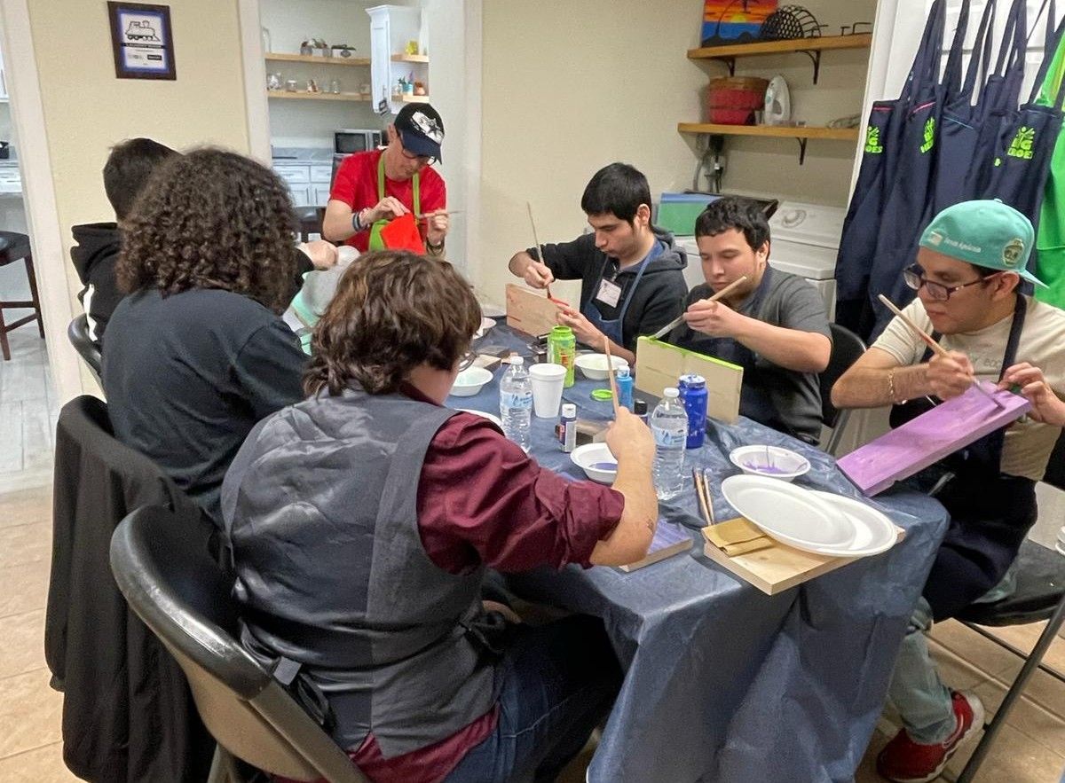 Group painting at a table: Young people, colors, brushes, aprons. Indoors, creative activity.