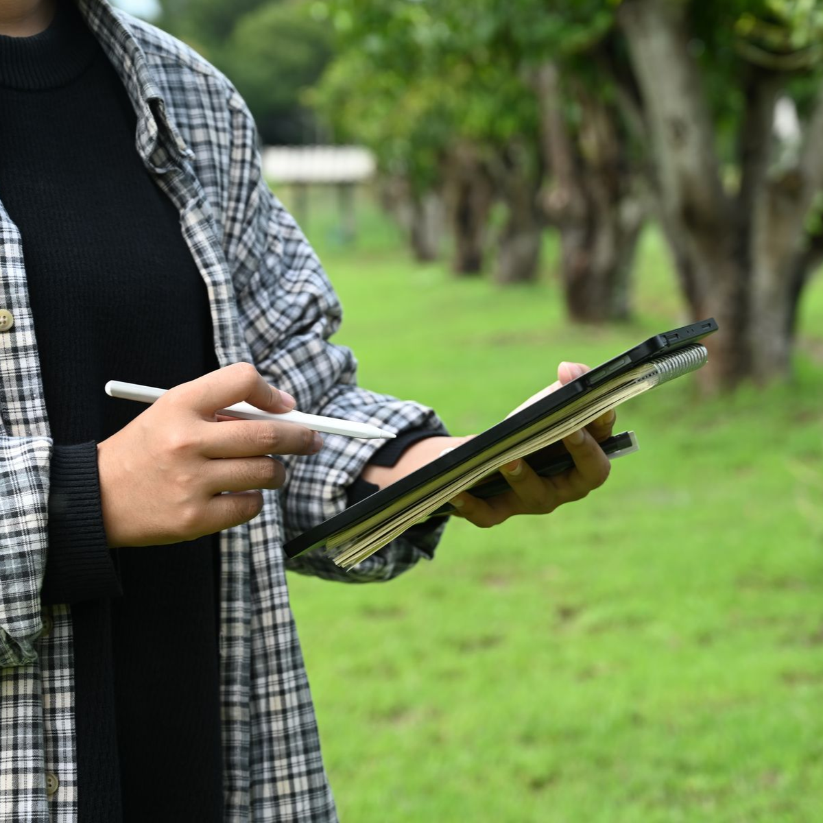 Person writing on a tablet outdoors in a green park