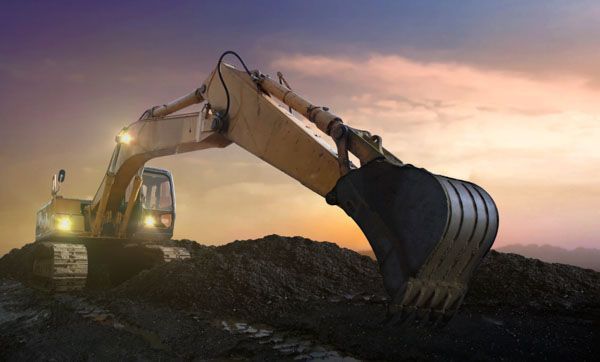 An excavator is digging a pile of dirt in a construction site at sunset.
