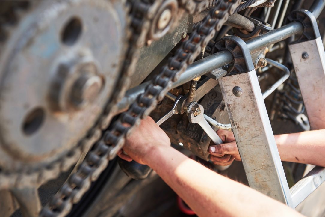 A person is working on a motorcycle chain with a wrench.