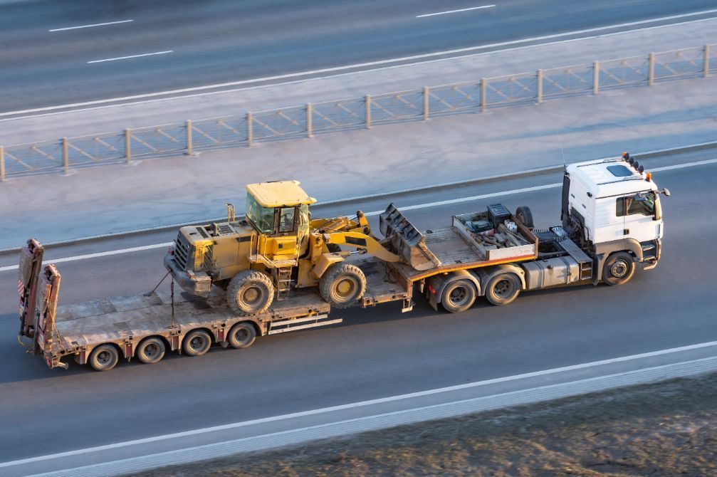 A truck is carrying a bulldozer on a trailer on a highway.