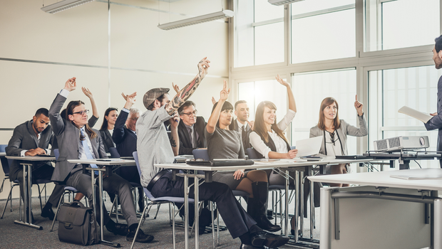 People in a classroom raising hands to answer a question; a presenter stands near a projector and window.