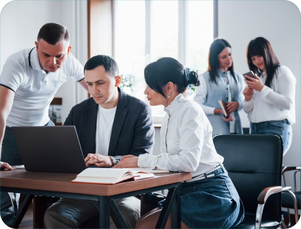Business team collaborates at a table with a laptop, books, and casual attire.
