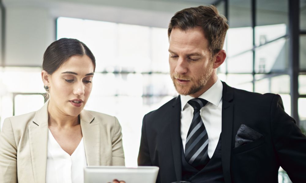 Woman and man in business attire looking at a tablet in a modern office.