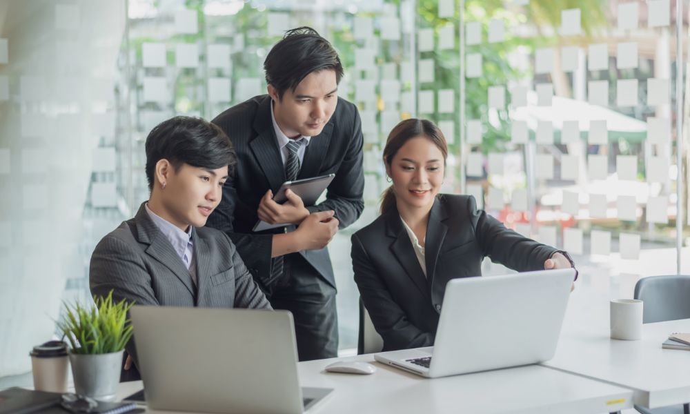 Three businesspeople looking at a laptop together at a modern office.