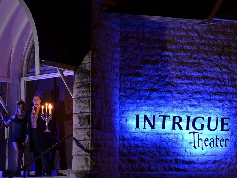 A couple of people standing in front of a building with a sign that says intrigue theater.