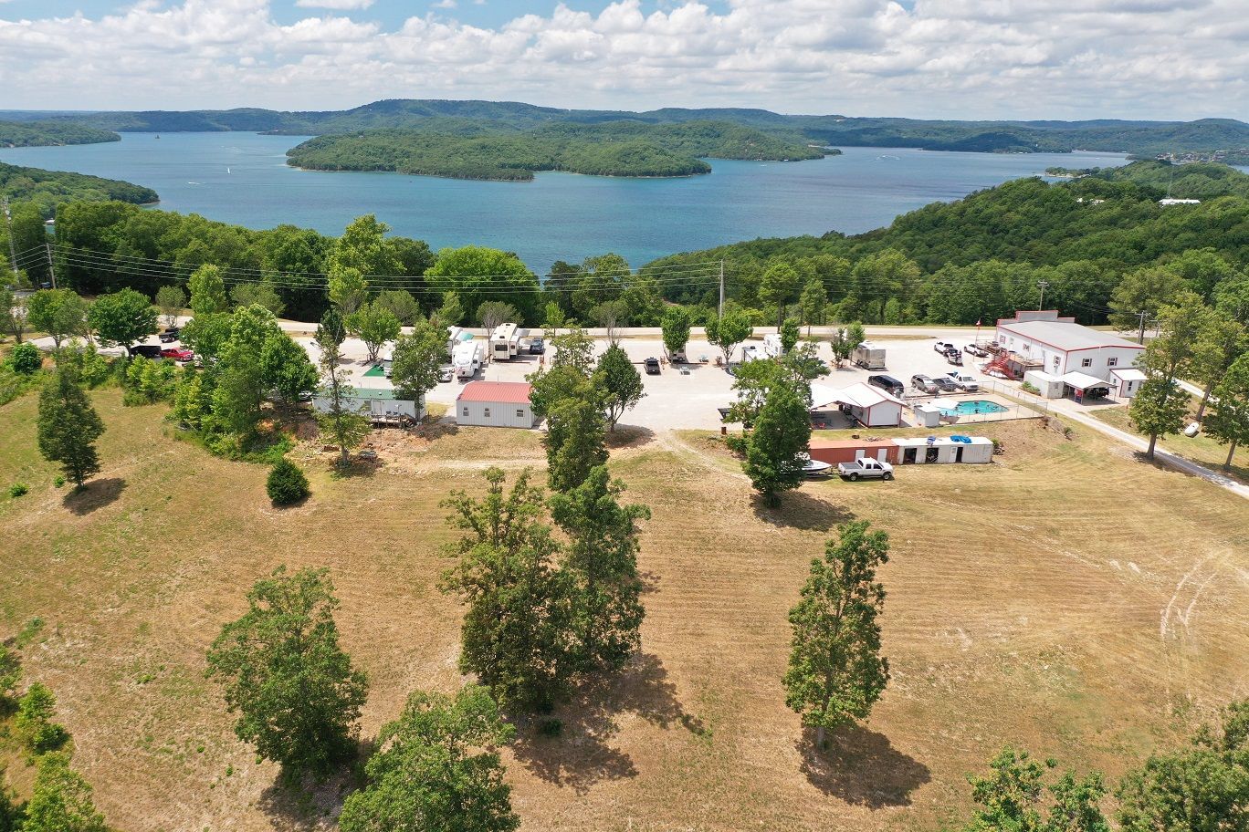 Aerial view of a lakeside campground with trees, cabins, and a blue lake in the background.