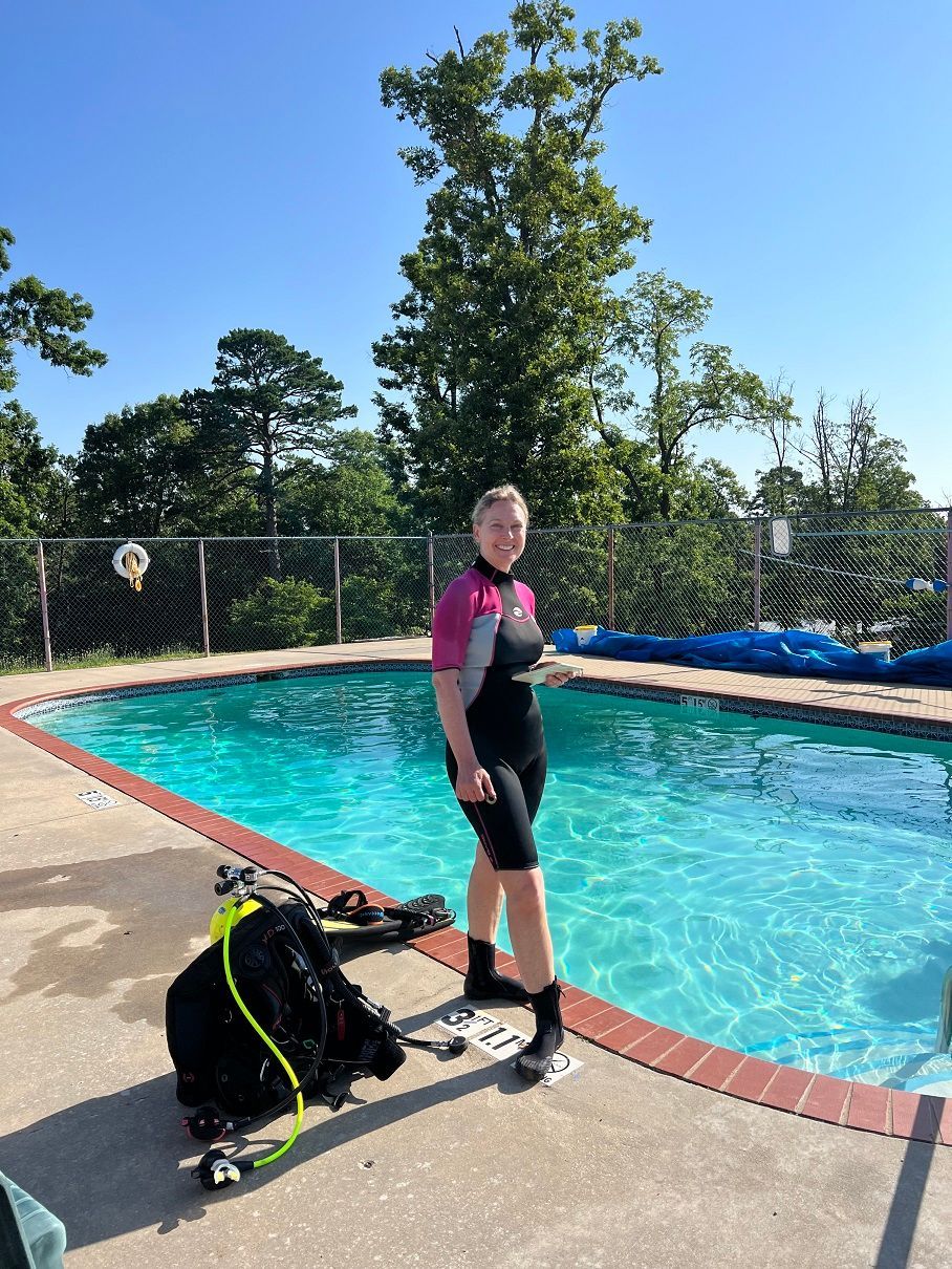 Kathy in a wet suit is standing next to a swimming pool.